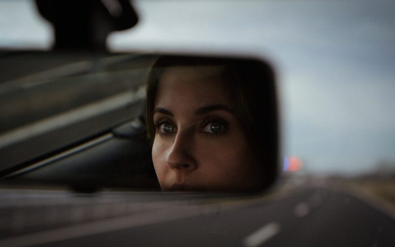 a woman's reflection in the side view mirror of a car